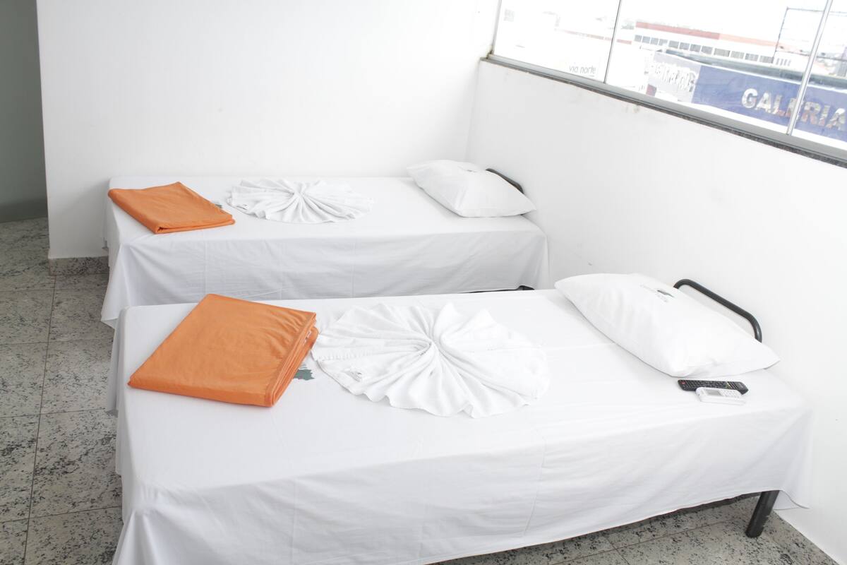 Two single beds with white and orange bedding, a remote control, and a pillow on one bed.