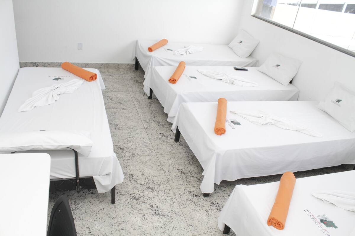 A hotel room with four single beds, each with a white sheet and an orange towel.