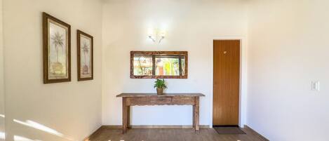 A hallway with a wooden bench, framed artwork, a mirror, and a door.