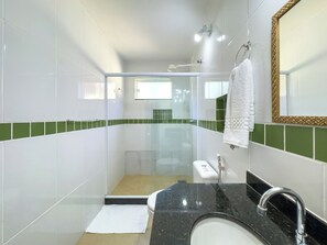 Een moderne badkamer met een douchecabine van glas, een wit wastafelmeubel met een zwart aanrechtblad en een spiegel met gouden lijst.