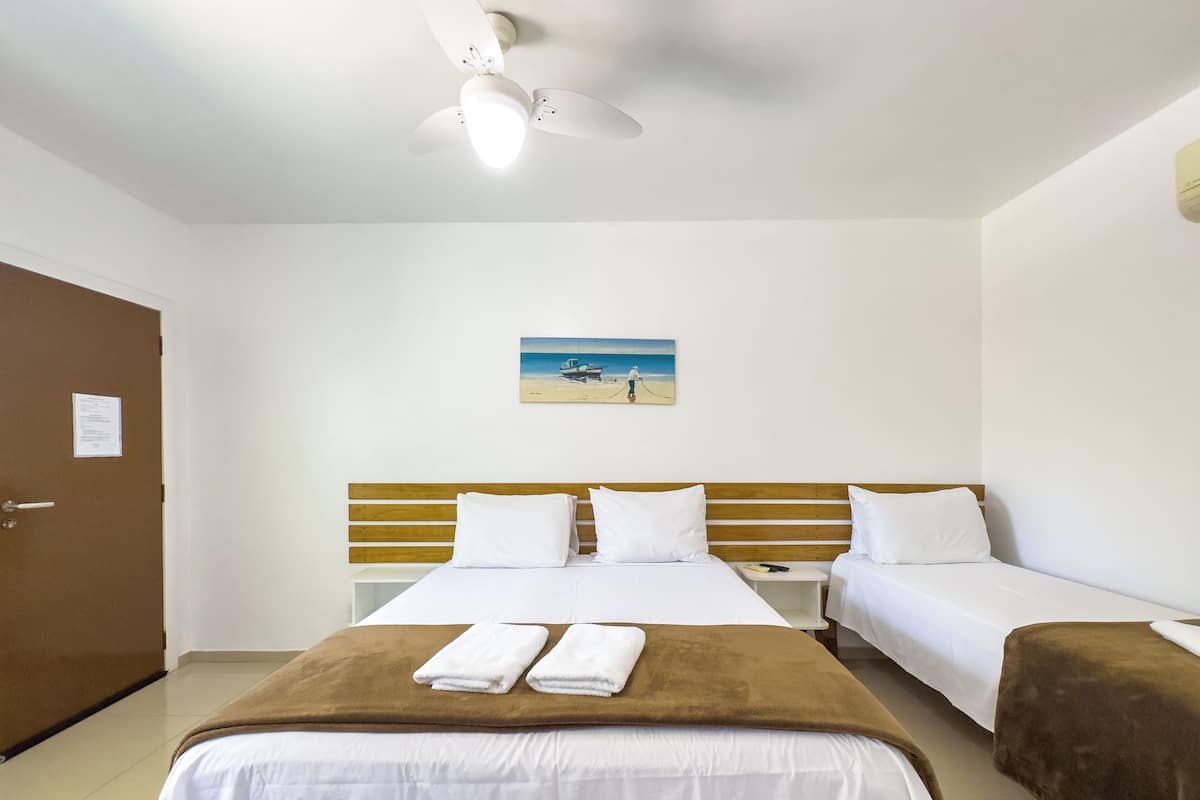 Hotelkamer met een groot bed, twee kleinere bedden, een plafondventilator en een schilderij van een strandgezicht.
