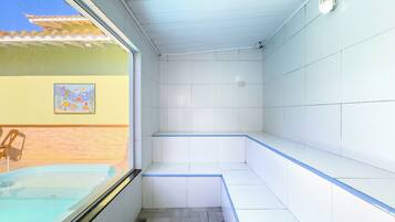 Un baño con suelo de baldosas, zona de ducha y ventana con vistas a una piscina.