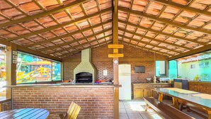 An outdoor patio with a brick fireplace, wooden tables and benches, and a view of a playground. - Pousada Sonho de Geribá (Búzios)