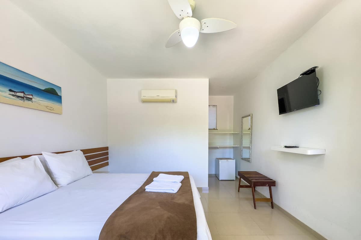 Een hotelkamer met een bed, een plafondventilator, een aan de muur bevestigde televisie en een tafeltje.