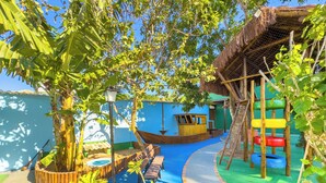 A children's play area with a blue and green floor, a hammock, a small boat, and a climbing structure. - Pousada Sonho de Geribá (Búzios)