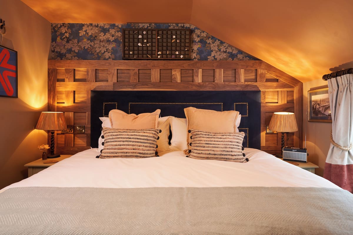 A large bed with a wooden headboard, two bedside tables with lamps, and a floral-patterned wall above the bed.