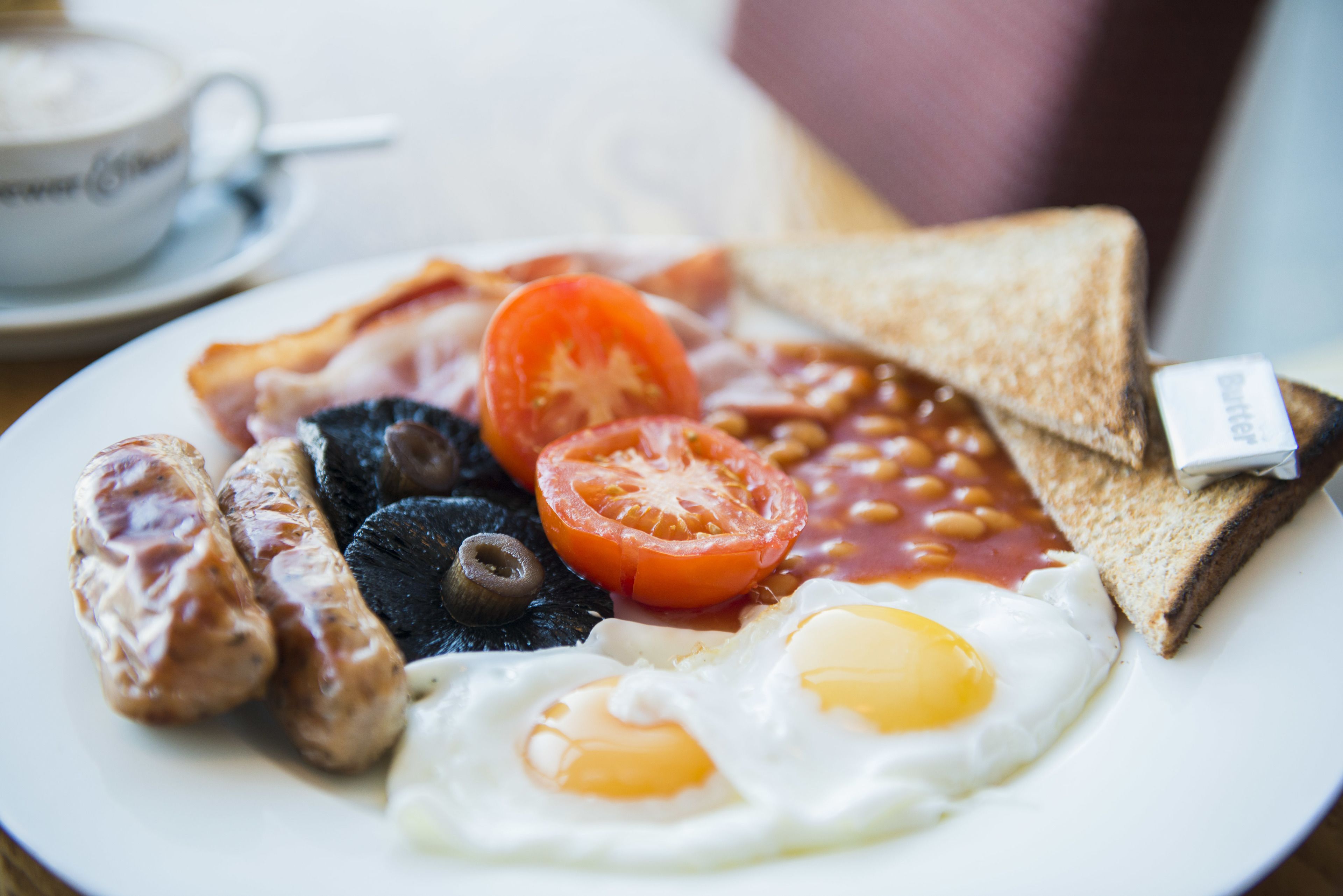 A plate of breakfast with eggs, sausages, tomatoes, beans, toast, and a cup of coffee.