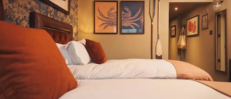 Een hotelkamer met twee bedden, een hoofdeinde, kunstwerken in lijsten en een potplant.