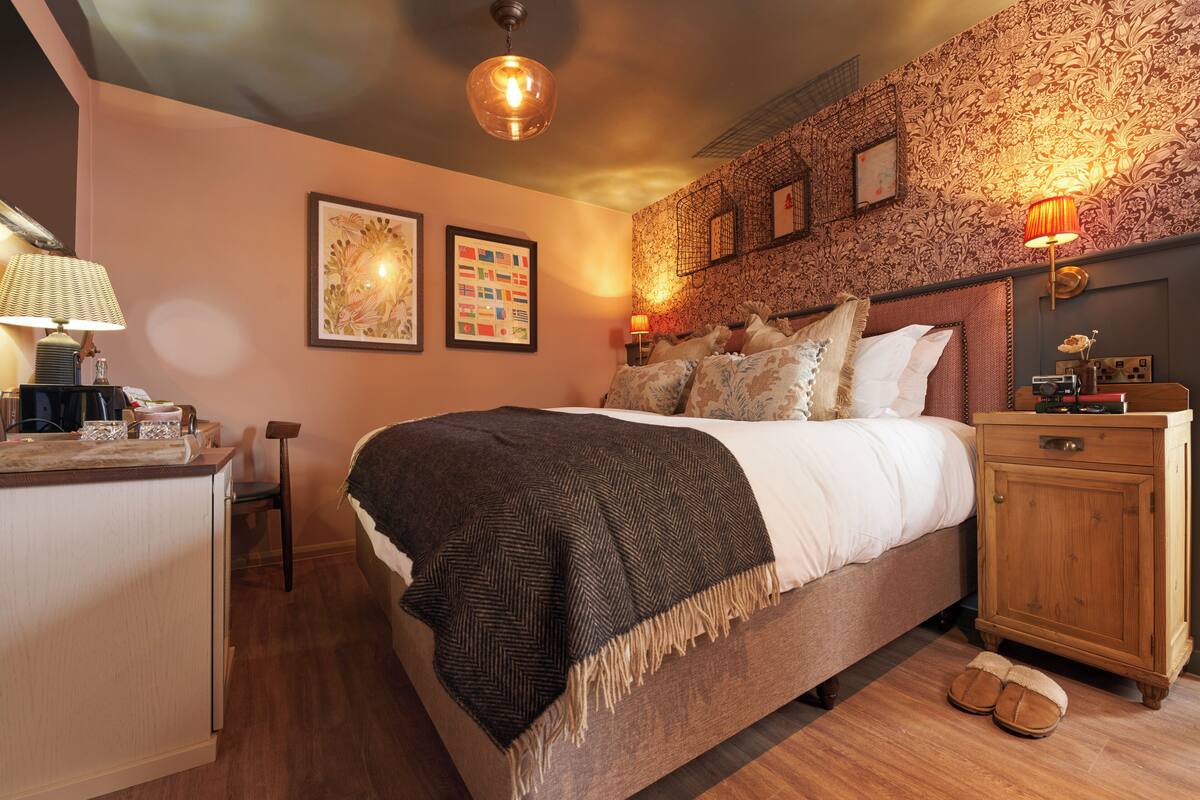 A neatly arranged bedroom with a bed, bedside table, lamp, and a small desk with a chair.