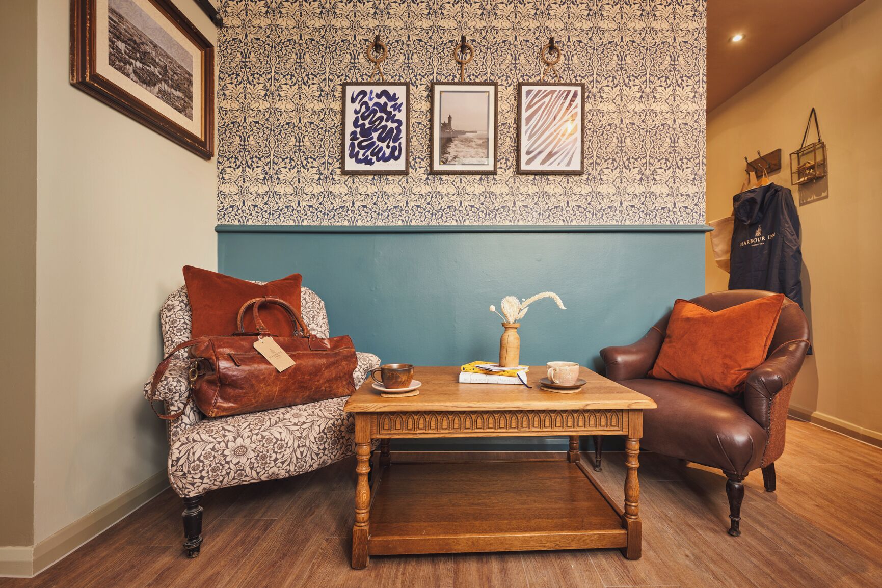 A room with a patterned wallpaper, a wooden coffee table, a leather armchair, and a sofa with a floral cushion.
