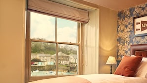 A hotel room with a large window, a bed with a headboard, a lamp, and a floral wallpaper.