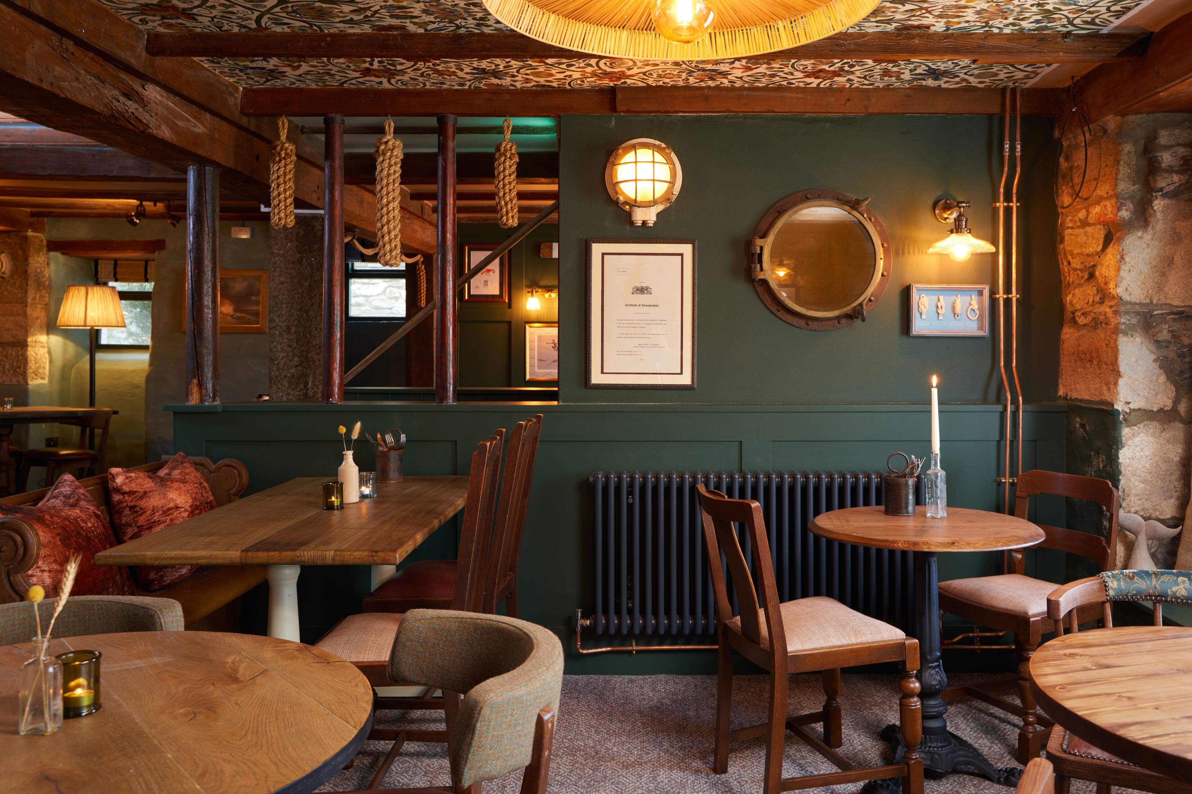 Interior acogedor de un restaurante con mesas y sillas de madera, una pared verde y un techo de estilo vintage.
