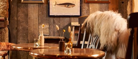 A rustic wooden interior with a round table, chairs, and framed artwork on the walls.