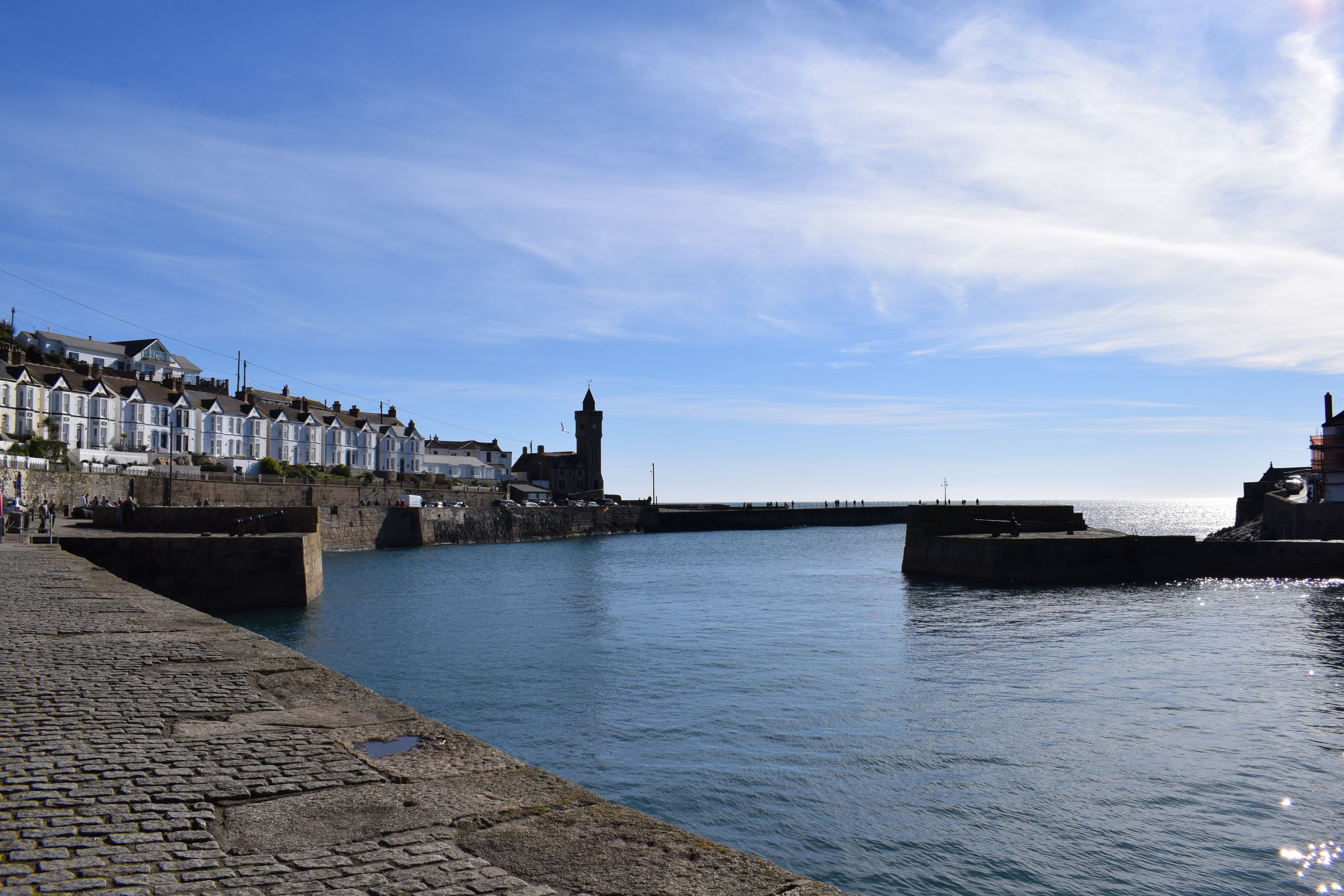A waterfront promenade with stone piers, a historic tower, and terraced houses.