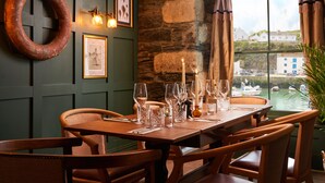 A dining table set with wine glasses and candles, a wooden chair, and a view of a harbor with boats.