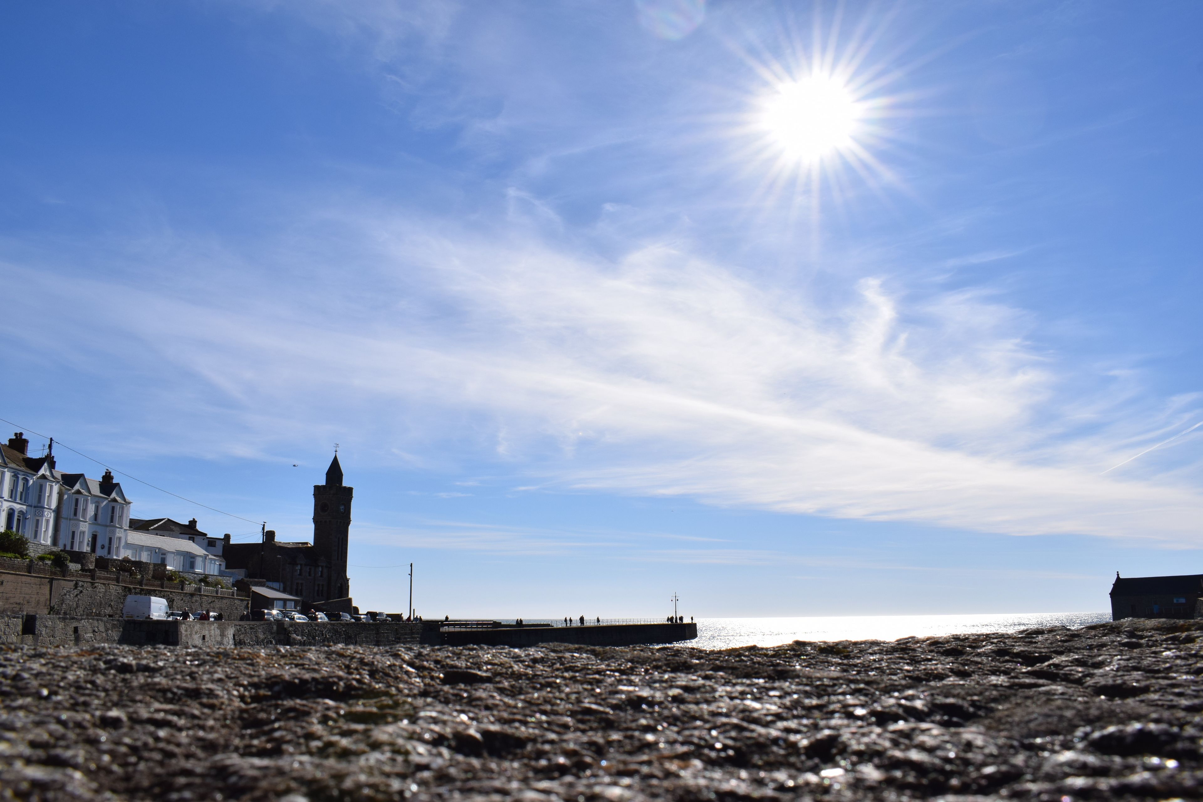 A coastal scene with a rocky beach, a pier, and buildings including a tower.