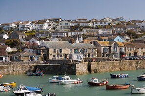 A coastal town with a stone wall, a variety of boats docked in the water, and a mix of residential buildings in the background. - Harbour Inn (Helston)