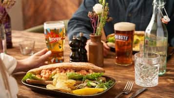A dining table with a sandwich, a beer glass, a bottle, and a glass of water.