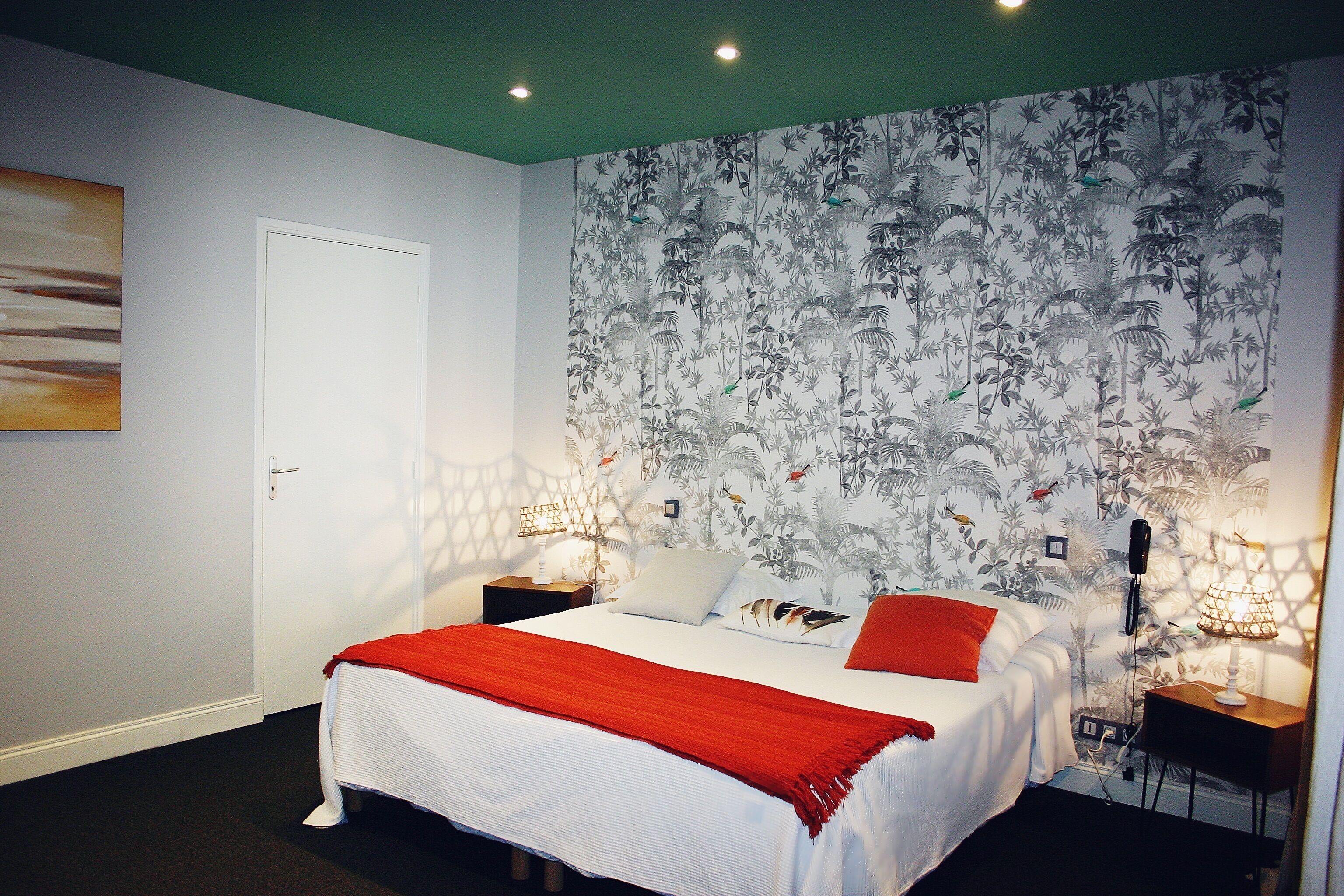 A bedroom with a bed, nightstands, a desk, and a wall with a floral pattern.