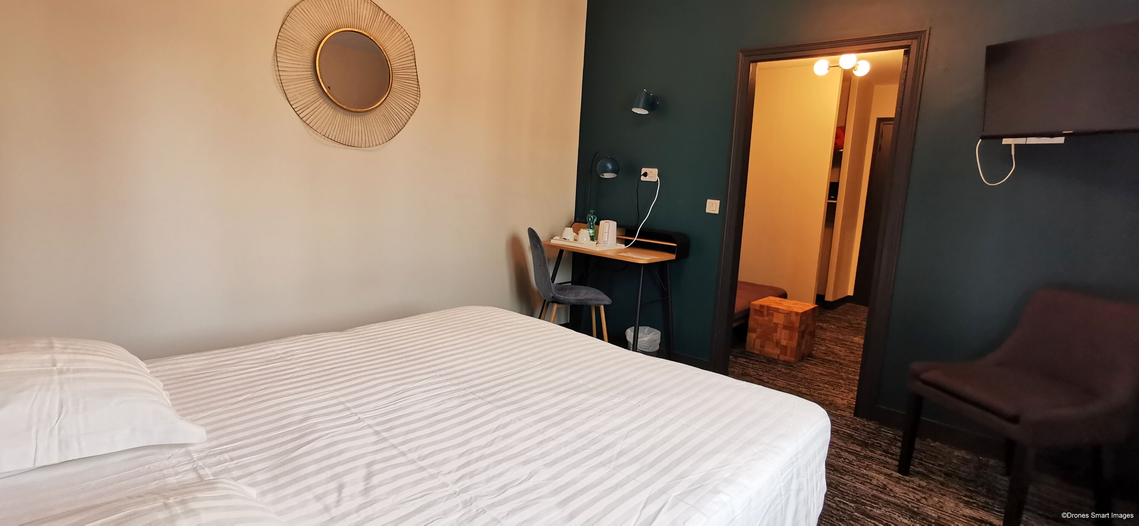 Une chambre d’hôtel avec un lit, un bureau avec une chaise, un petit tabouret et un miroir au mur.