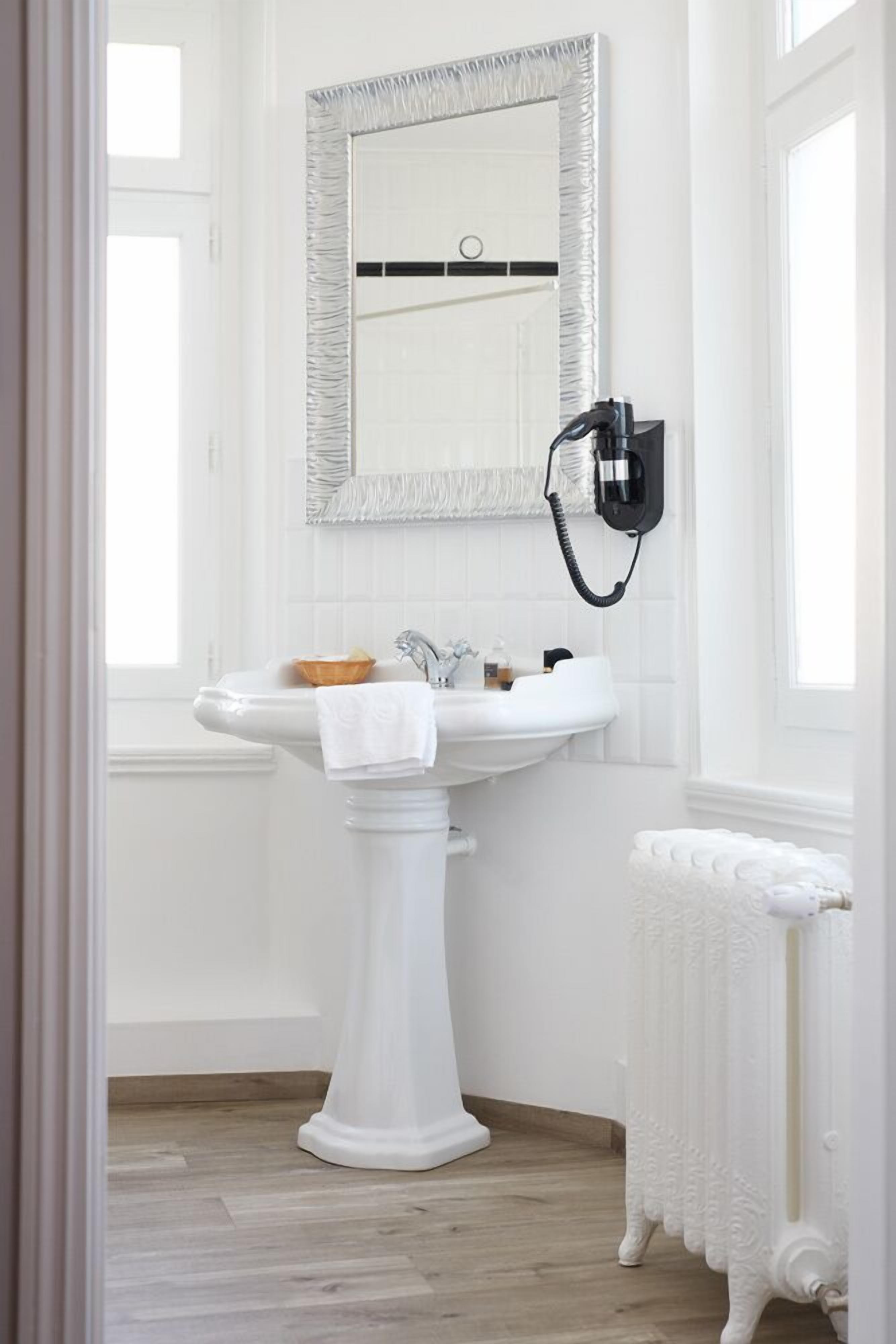 A white pedestal sink with a towel, a mirror with a textured frame, and a wall-mounted hairdryer.