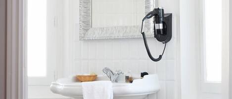 A white pedestal sink with a towel, a mirror with a textured frame, and a wall-mounted hairdryer.