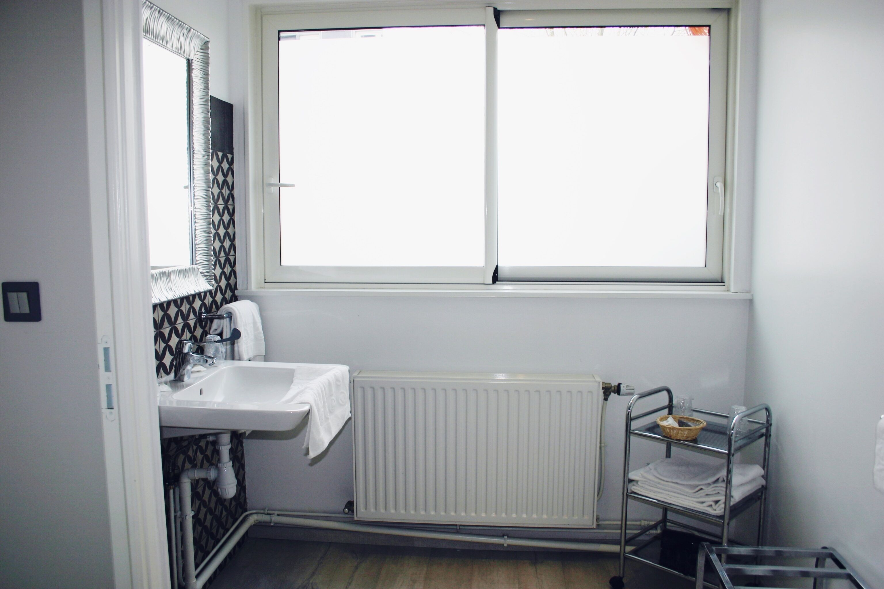 A bathroom with a white sink, a mirror, a window, and a radiator.