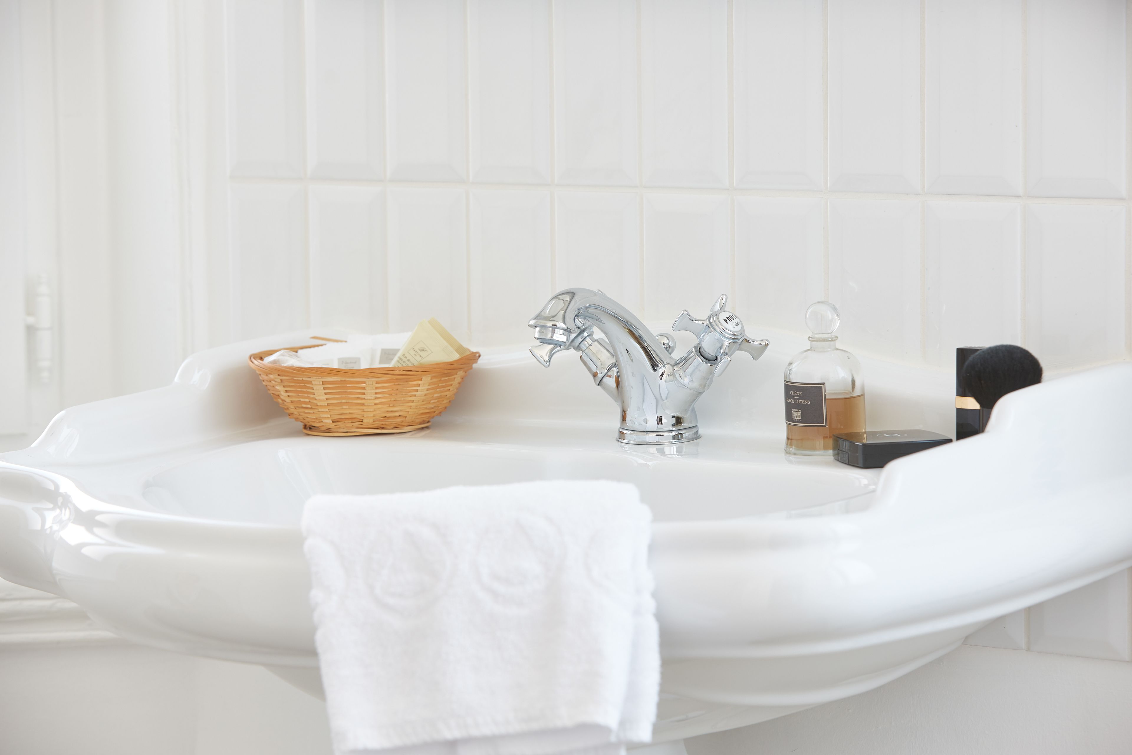 A bathroom with a white sink, a silver faucet, a wicker basket, and a white towel.