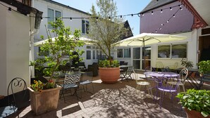 An outdoor patio with tables and chairs, potted plants, and string lights. - The Originals Boutique, Hôtel La Colonne de Bronze (Saint-Valery-sur-Somme)