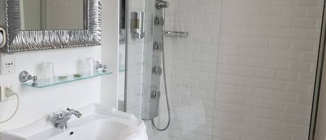 Un baño con lavamanos pedestal blanco, cabina de ducha de vidrio y un espejo grande con marco metálico.
