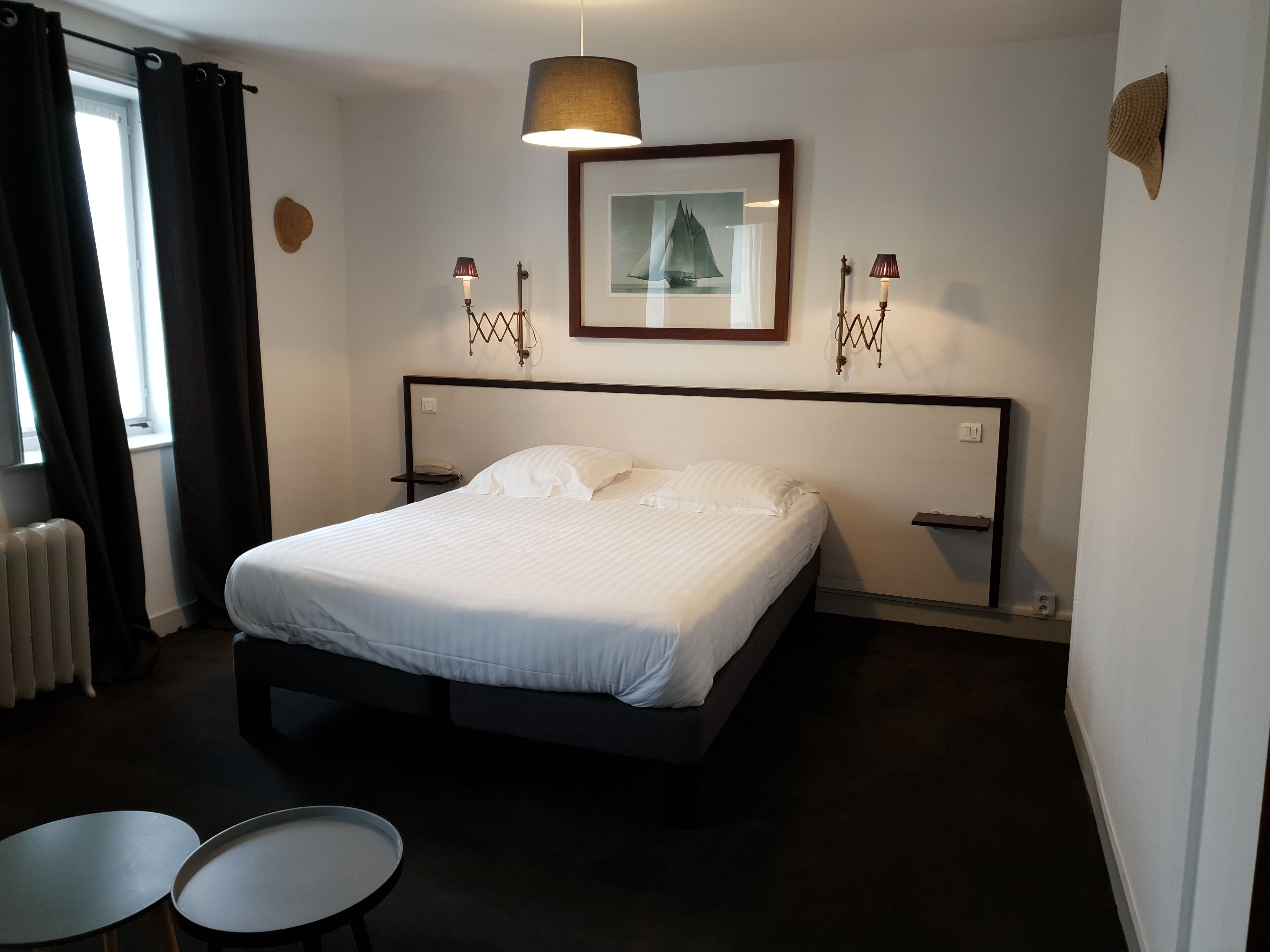 Een netjes opgemaakt bed in een hotelkamer, met een ingelijst beeld aan de muur, twee nachtkastjes en een radiator.