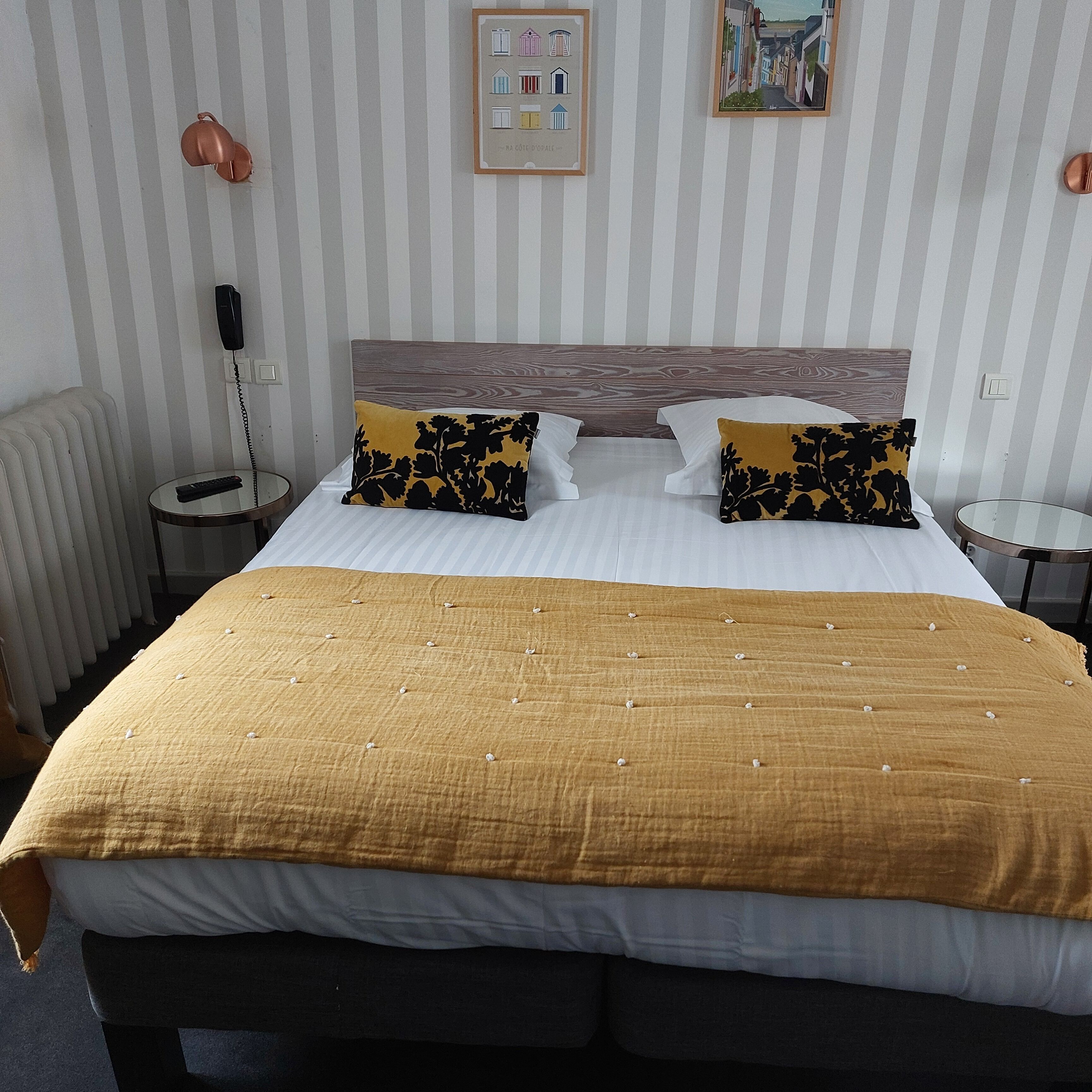 Ein Hotelzimmer mit einem großen Bett, zwei Nachttischen, einem Telefon, einem Heizkörper und zwei gerahmten Bildern an der Wand.