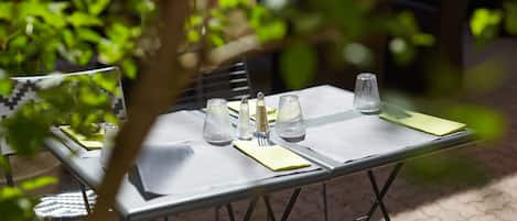 Una mesa al aire libre con estructura metálica, un florero de vidrio y un mantel individual verde.