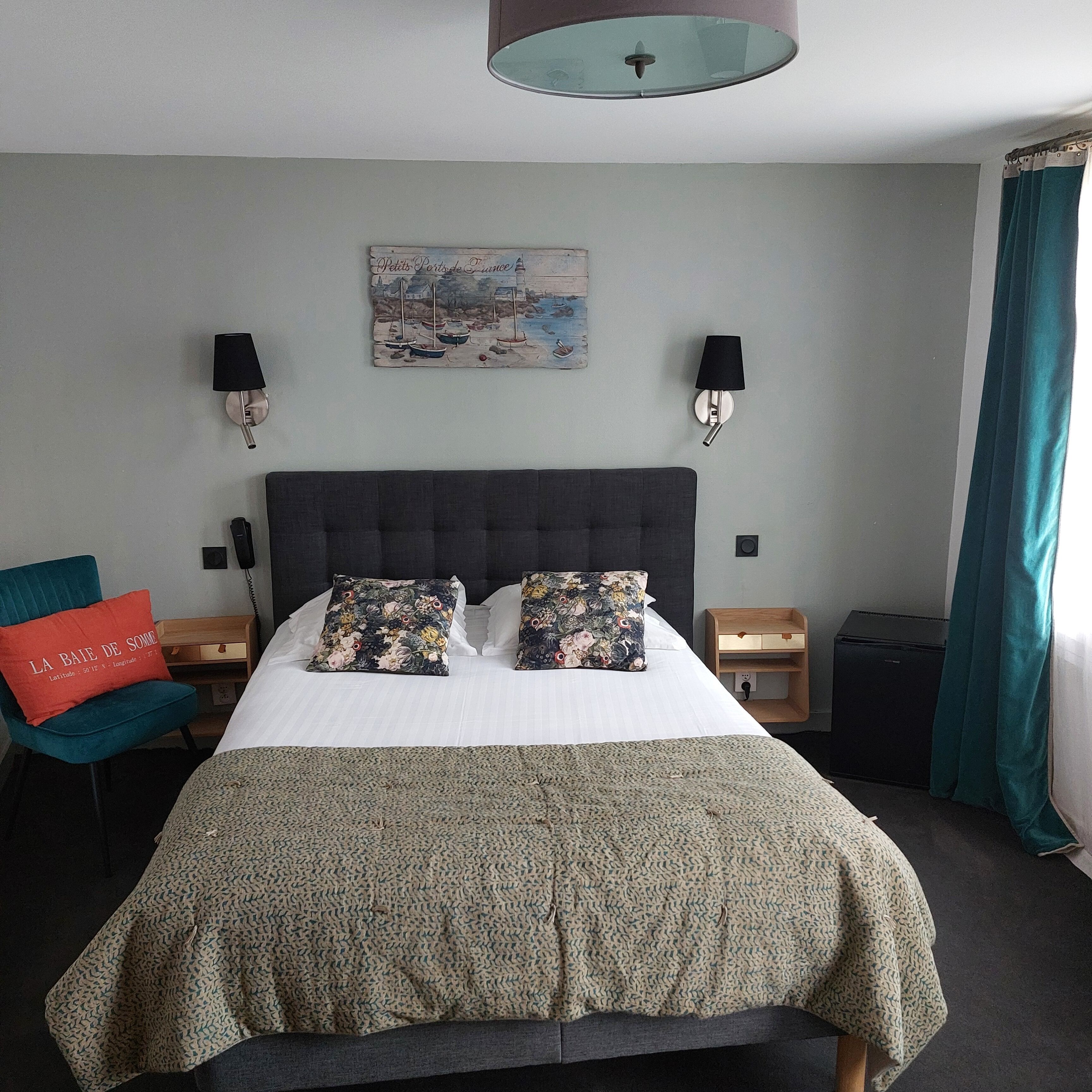 Une chambre bien rangée, avec un grand lit, deux tables de chevet, une commode, un fauteuil rouge et un tableau accroché au mur.