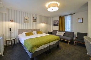 A hotel room with a bed, a sofa, a chair, a lamp, and a picture on the wall. - The Originals Boutique, Hôtel La Colonne de Bronze (Saint-Valery-sur-Somme)