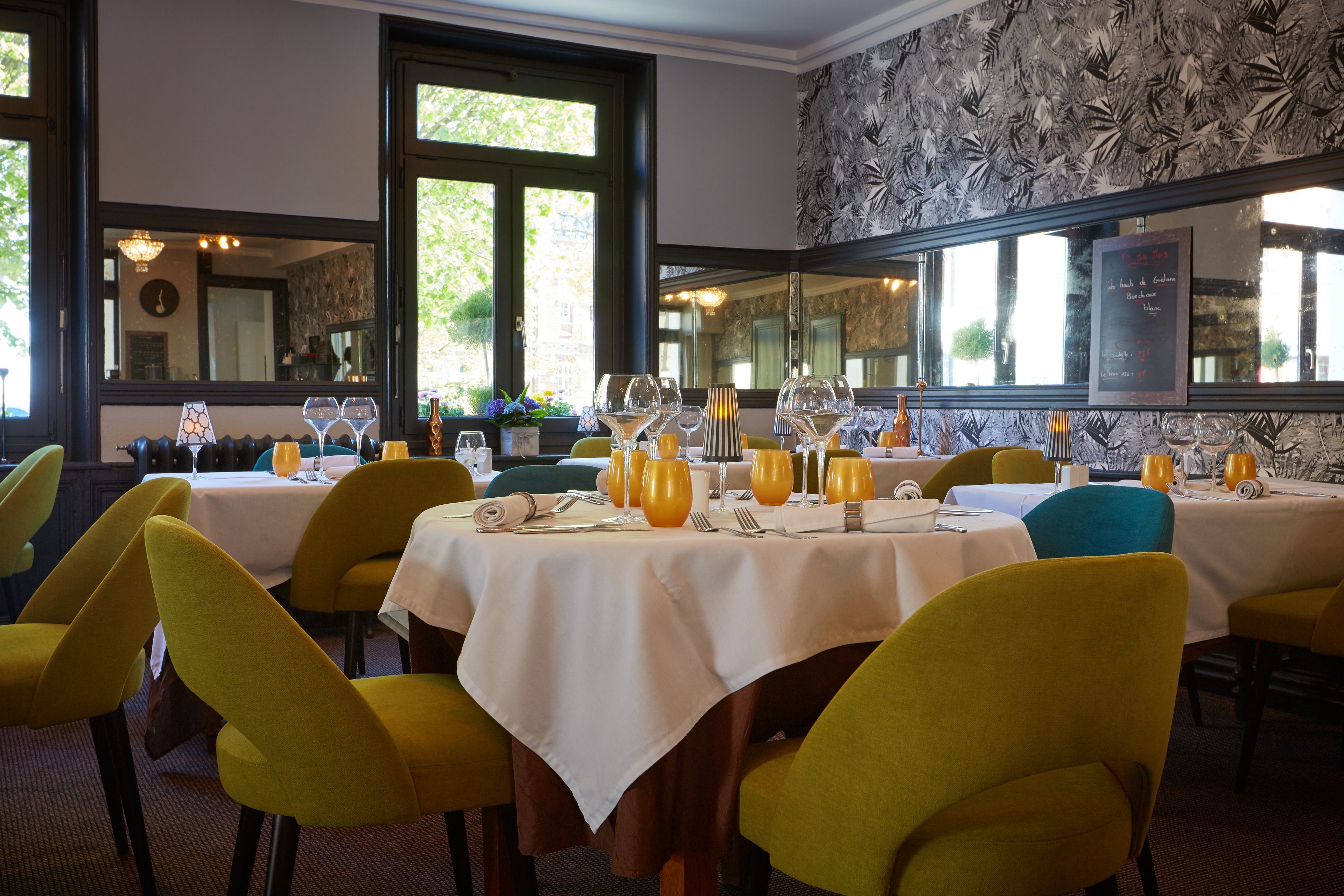 A dining area with tables set for four, yellow chairs, and a large mirror on the wall.