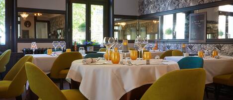 A dining area with tables set for four, yellow chairs, and a large mirror on the wall.