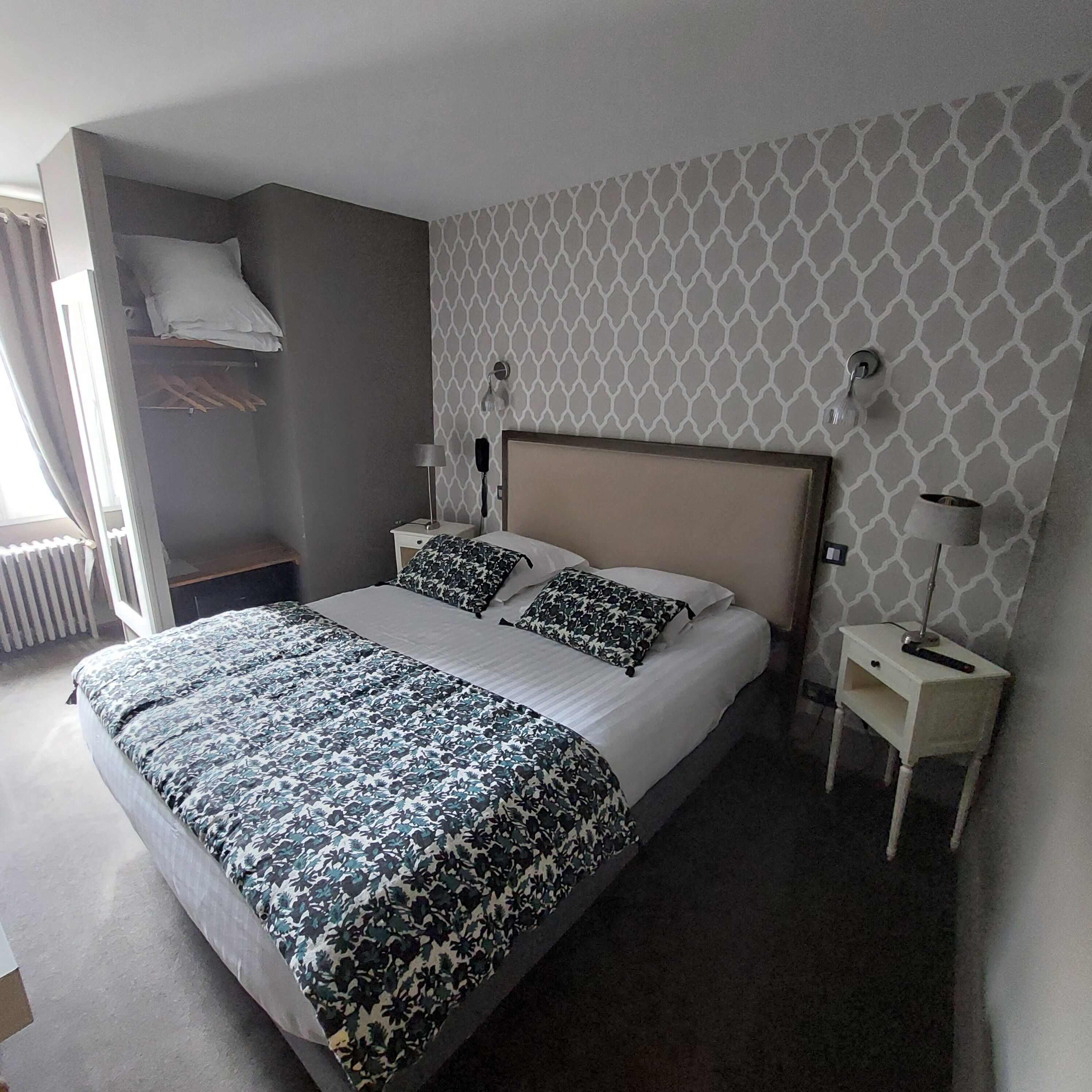 A neatly made bed with a patterned bedspread, a bedside table with a lamp, and a wall with a geometric pattern.