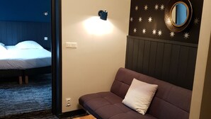 A room with a sofa, a small wooden table, a wall-mounted light, and a star-patterned wall. - The Originals Boutique, Hôtel La Colonne de Bronze (Saint-Valery-sur-Somme)