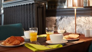 A breakfast setting with croissants, orange juice, and toast on a table with a lamp and a marble wall in the background. - The Originals Boutique, Hôtel La Colonne de Bronze (Saint-Valery-sur-Somme)