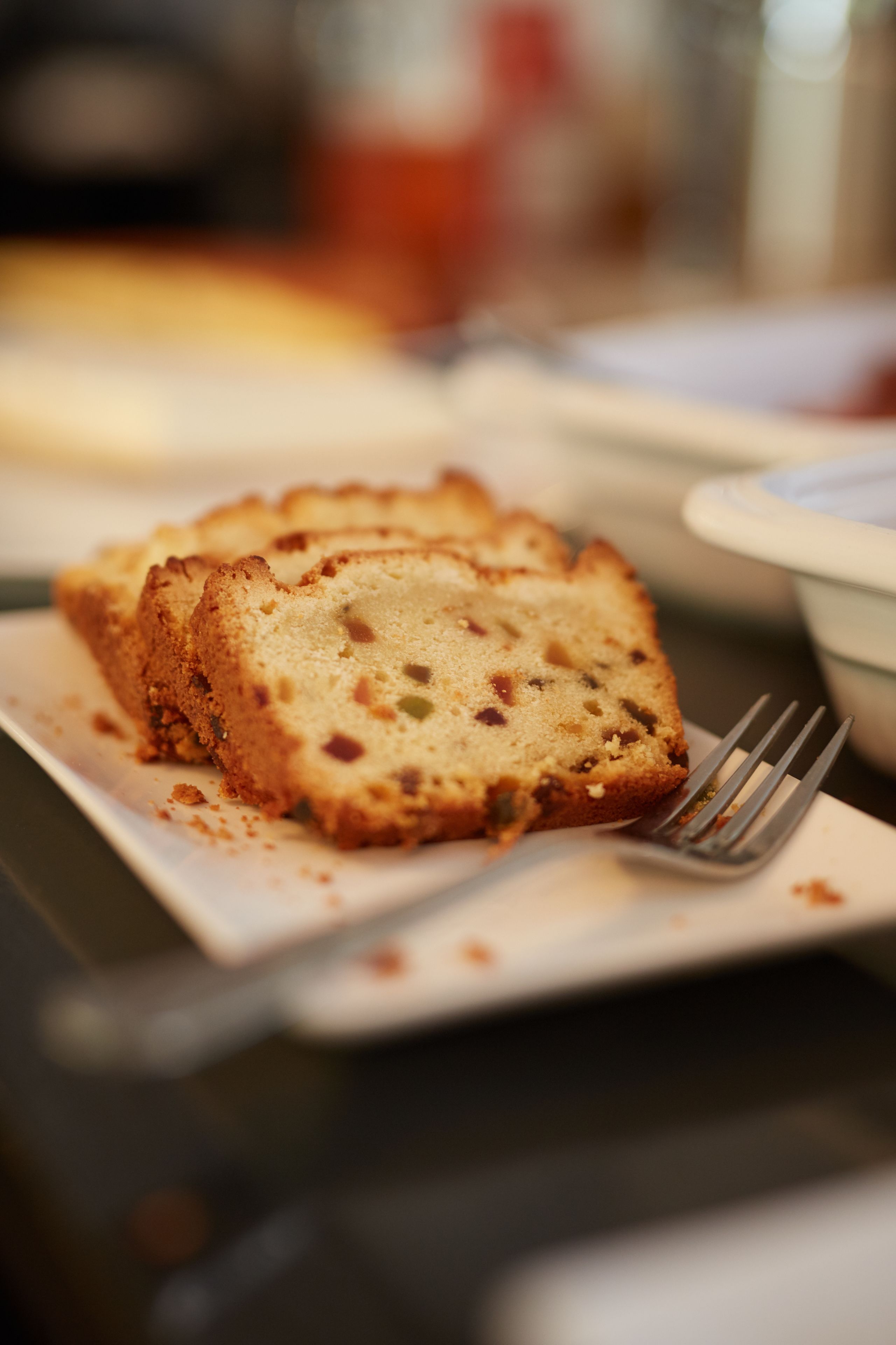A slice of fruitcake on a white plate with a fork beside it.
