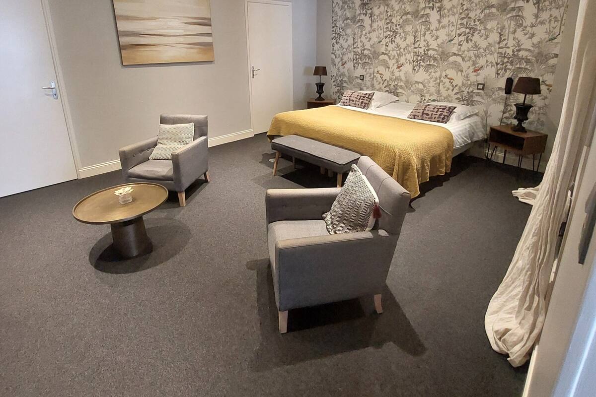Une chambre à coucher comprenant un lit, deux fauteuils, une petite table et une table de chevet avec des lampes.