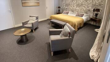 A bedroom with a bed, two armchairs, a small table, and a nightstand with lamps.