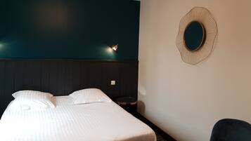 A hotel room with a bed, a nightstand, a chair, and a wall-mounted mirror.