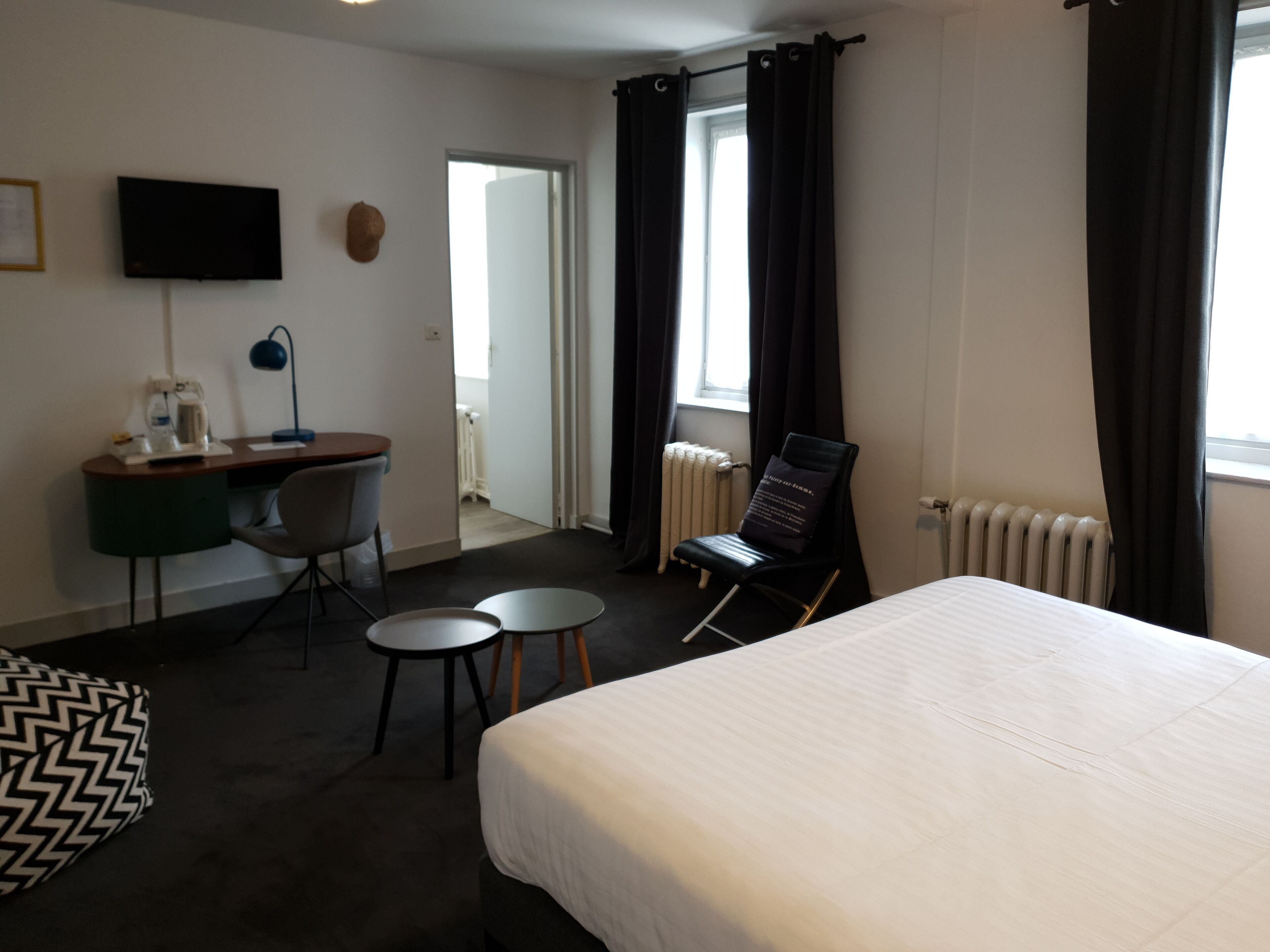 A hotel room with a bed, a desk with a chair, a television, and a window with curtains.