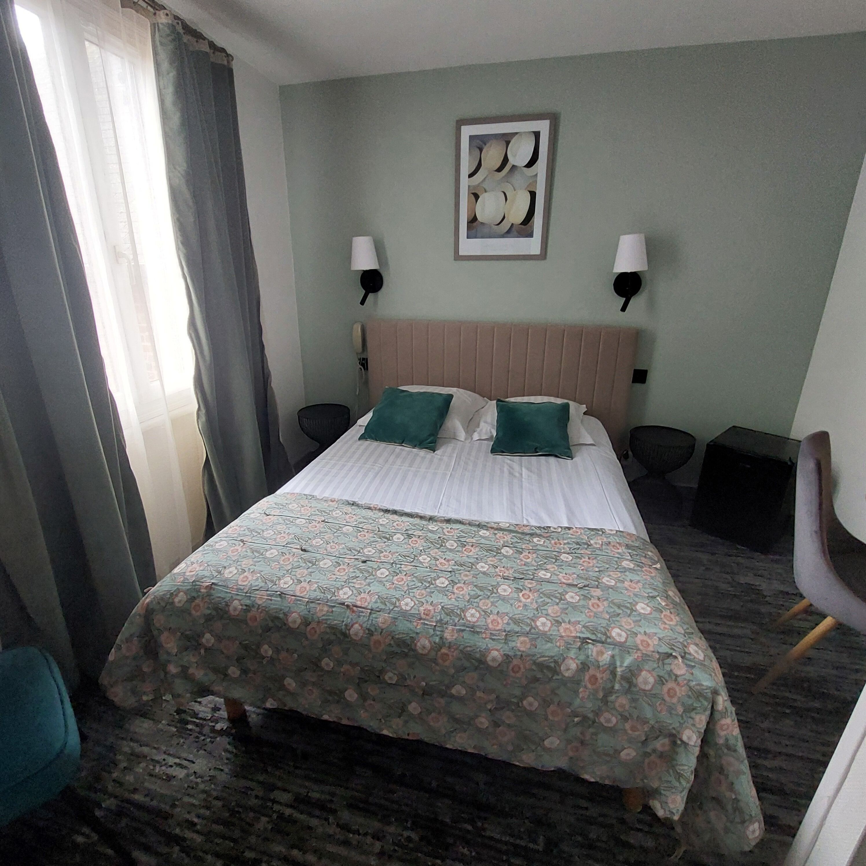 A hotel room with a bed, two bedside lamps, a headboard, a framed picture on the wall, and a window with curtains.