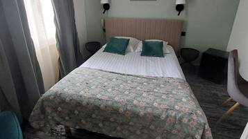 A hotel room with a bed, two bedside lamps, a headboard, a framed picture on the wall, and a window with curtains.