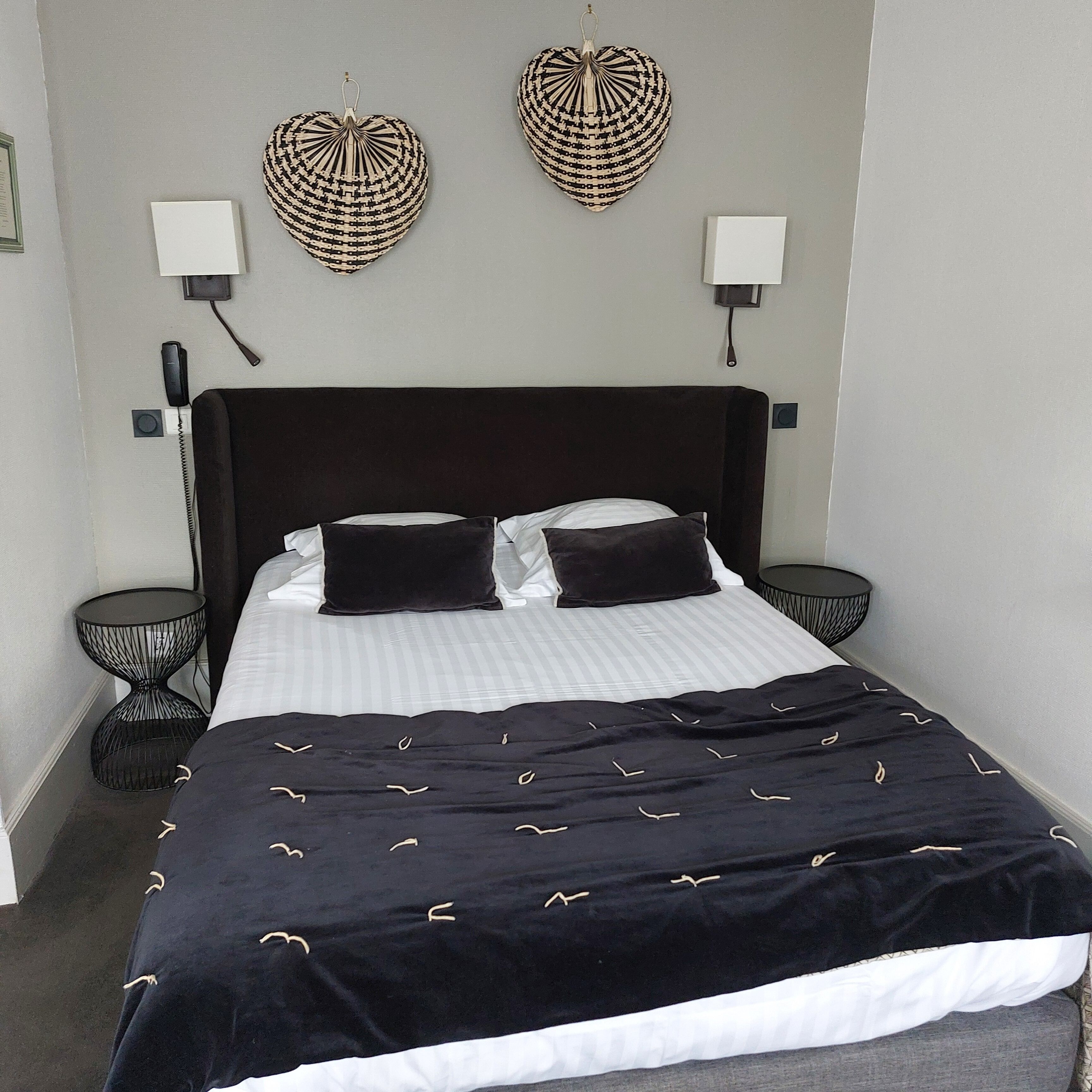 A neatly made bed with a black and white striped duvet, two black pillows, and a black headboard. There are two black nightstands with woven baskets on them.