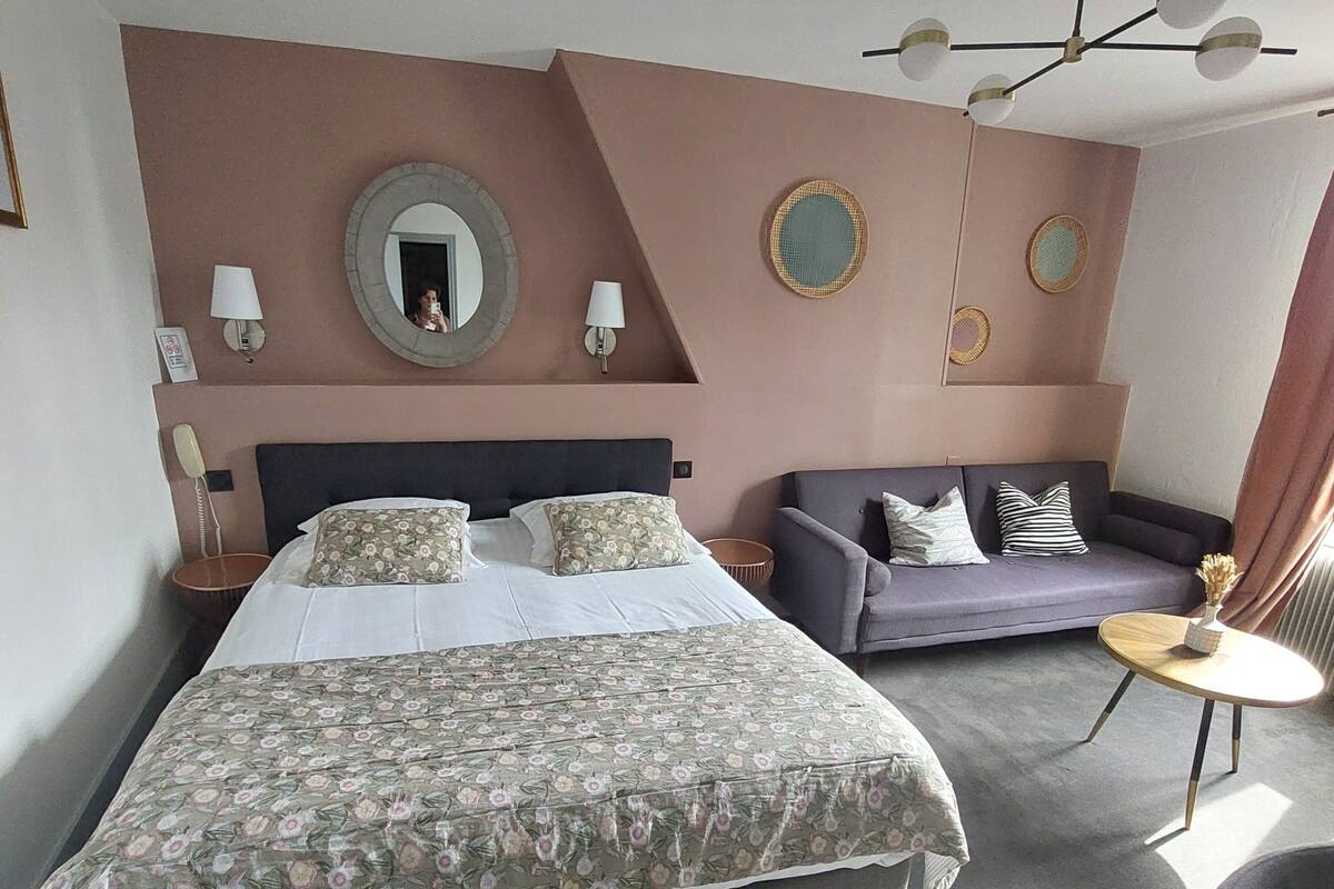 Une chambre d’hôtel avec un grand lit, un canapé, une petite table et un luminaire fixé au plafond.