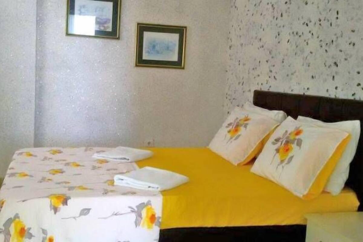 A bedroom with a bed, floral bedspread, pillows, and a nightstand.